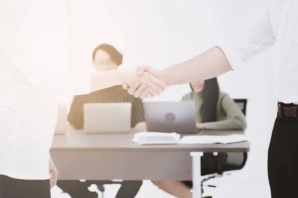 Successful work handshake. Business man and woman shaking hand together with their team in background. Muted tone.