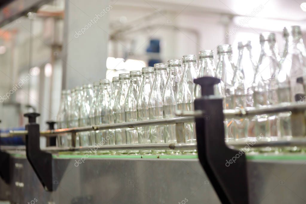 Beverage production line background. A conveyor belt full of empty glass bottle going into bottle filling machine. Beverage manufacturing concept.