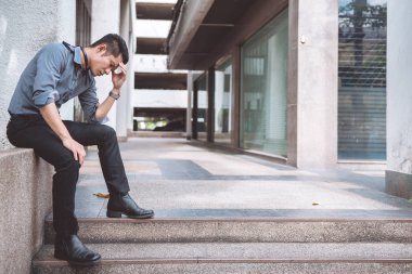 Sokakta oturan işsiz adam. Asya adam stres bakarak ve ofis binası arka plan ile duygusal.