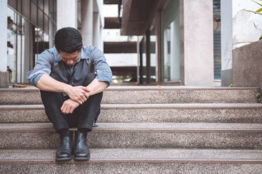 Sokakta oturan işsiz adam. Asya adam stres bakarak ve ofis binası arka plan ile duygusal.