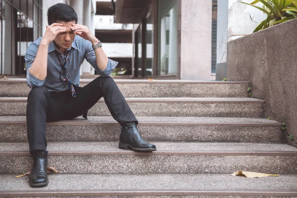 Unemployed man sitting on the street. Asia man looking stress and emotional with office building background.