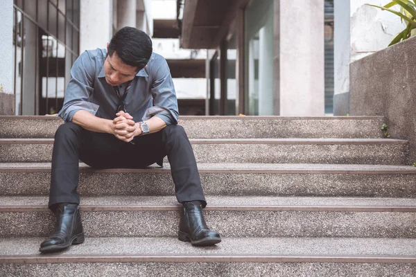 Unemployed man sitting on the street. Asia man looking stress and emotional with office building background.