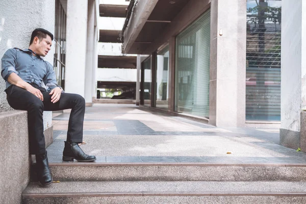 Unemployed man sitting on the street. Asia man looking stress and emotional with office building background.