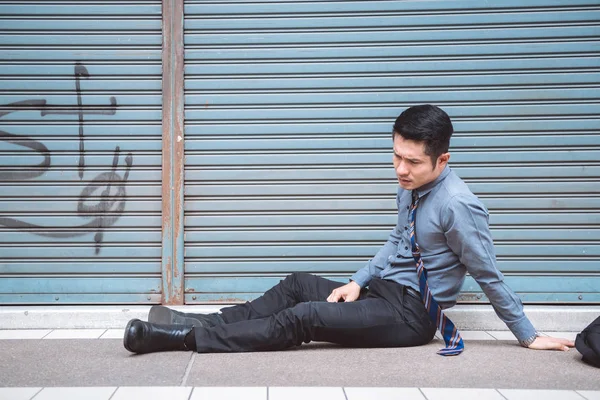 Unemployed man sitting on the street. Asia man looking stress and emotional with closed store background.