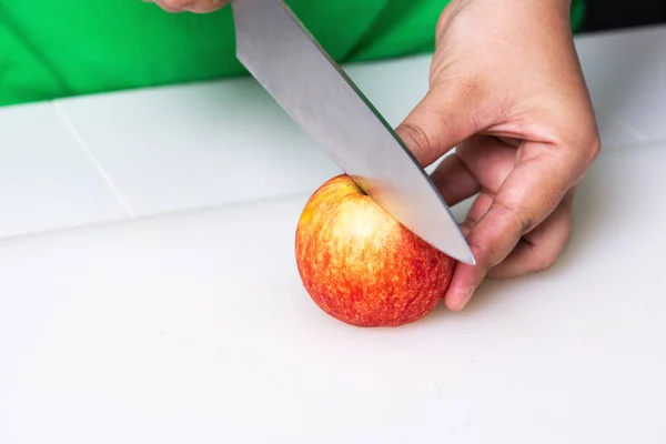 Woman trying to cut apple with chief knife. Asian woman in green tshirt. Cllose up shot.