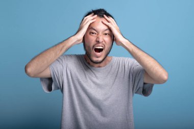 Genç adam heyecan şok edici poz mavi renkli sakallı. Çok ifade, yarım vücut vurdu şok edici Asya genç hippi ellerini kapak yüz, sürpriz. Genç nesil yenilikçi kavram. 