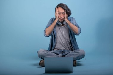 Genç adam oturup bilgisayarla mavi arka planda katta sakallı. tam vücut vurdu, dizüstü bilgisayar kullanarak şok Asya genç hippi. Genç nesil yenilikçi çalışma kavramı.