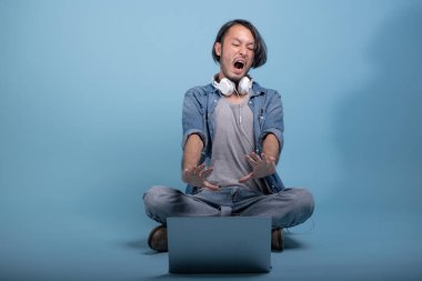 Genç adam oturup bilgisayarla mavi arka planda katta sakallı. Tam vücut vurdu, dizüstü bilgisayar kullanarak şok Asya genç hippi. Genç nesil yenilikçi çalışma kavramı.