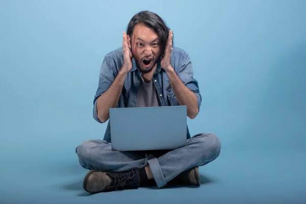 若いひげを生やした男は青い背景にコンピューターを使用して床に座る 狂牛病アジア若い流行に敏感 全身ショットのラップトップを使用します 若い世代の流行に敏感な働くコンセプト — ストック写真