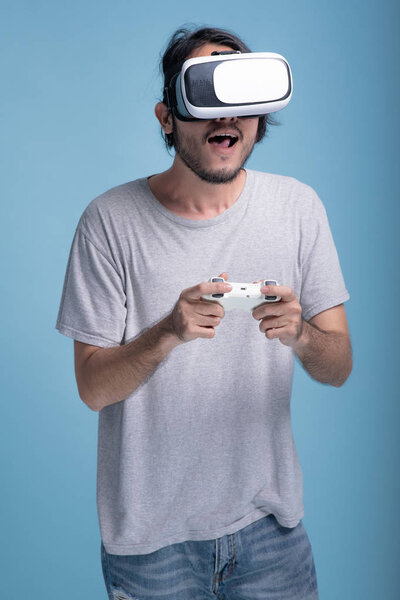 Young bearded man playing VR game in blue background. Shock Asian young hipster wearing VR headset, half body shot. Young generation hipster relaxation concept.