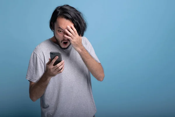 Возбужденный Бородатый Молодой Человек Смотрит Мобильное Сообщение Синем Фоне Азиатский — стоковое фото