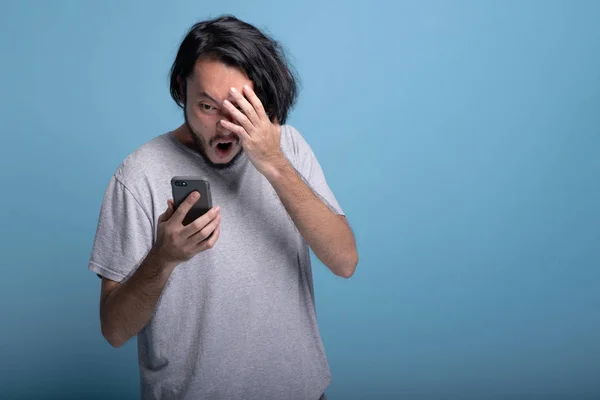 Opgewonden Young Bebaarde Man Kijken Naar Mobiel Bericht Blauwe Achtergrond — Stockfoto