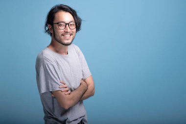 Genç sakallı adam kendine güvenen portre mavi arka planda çapraz kol. Asya genç hipster ayakta çapraz kol, kendine güvenen gülümseme, yarım vücut vurdu. Genç nesil yenilikçi kavram.