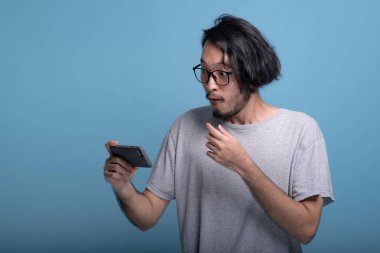 Sürpriz genç adam Mobil Oyunlar mavi arka planda çalmaya sakallı. Mobil oyun, yarım vücut vurdu iskambil Şok Asya genç hippi. Genç nesil yenilikçi rahatlatıcı kavramı.