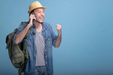 Genç adam gezgin mavi arka planda backpacking sakallı. Hareket eden telefon çağrısıyla arkadaşları, çok mutlu Asya genç hippi yarım vücut vurdu. Genç nesil yenilikçi tatil seyahat kavramı.