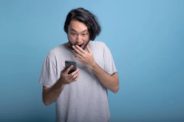 Jeune Homme Barbu Excité Regardant Message Mobile Arrière Plan Bleu — Photo