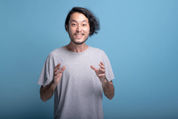 Young bearded man excited shocking pose in blue background. Shocked Asian young hipster mouth open wow pose, half body shot. Young generation hipster concept.