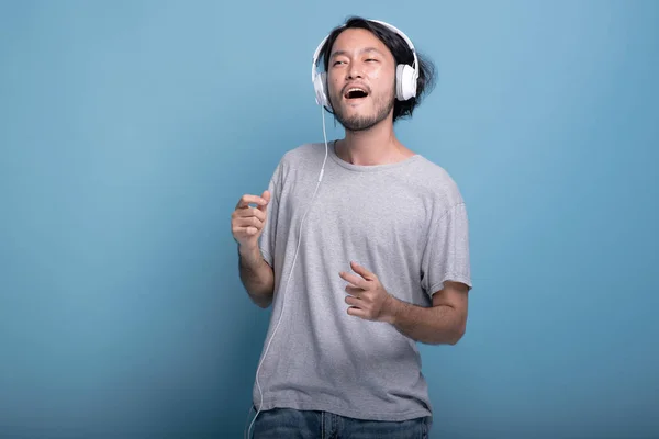 在蓝色背景下听音乐的年轻大胡子男子 非常高兴的亚洲年轻时髦使用白色耳机听和舞蹈音乐 半身体拍摄 年轻一代时髦的概念 — 图库照片