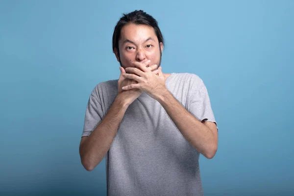 Young bearded man excited shocking pose in blue background. Shocked Asian young hipster with hands over mouth, exciting expression, half body shot. Young generation hipster concept.