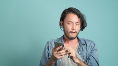 Genç erkek yenilikçi mobil ileti uygulama gelen kötü haber bulmak için seyir onun telefon sakallı. Asya adam cep telefonu arayan sıkılmış ve çok kızgın olarak o kötü haber mavi arka plan ile gördüm.