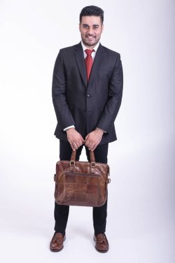 Beyaz arka planda izole iş adamı. Yakışıklı genç Hintli işadamı çanta portre ile takım elbiseli, kendine güvenen gülümseme görünüyor. Tam uzunlukta vurdu.