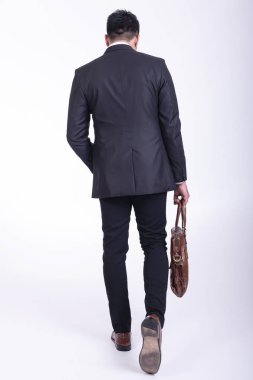 İzole iş adamı. Yakışıklı genç Hintli işadamı çanta portre ile takım elbiseli, elleri cebinde görünüyor gülümse. Tam uzunlukta geri vurdu.