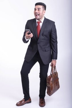 İzole iş adamı. Yakışıklı genç Hintli işadamı takım çantası üzerinde telefon portre, çok mutlu görünüyor. Tam uzunlukta vurdu.