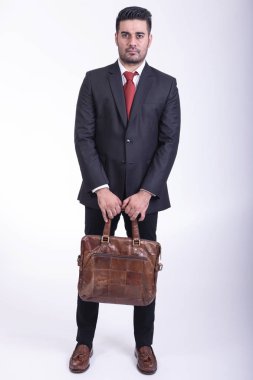 Beyaz arka planda izole iş adamı. Yakışıklı genç Hintli işadamı çanta portre ile takım elbiseli, kendine güvenen gülümseme görünüyor. Tam uzunlukta vurdu.