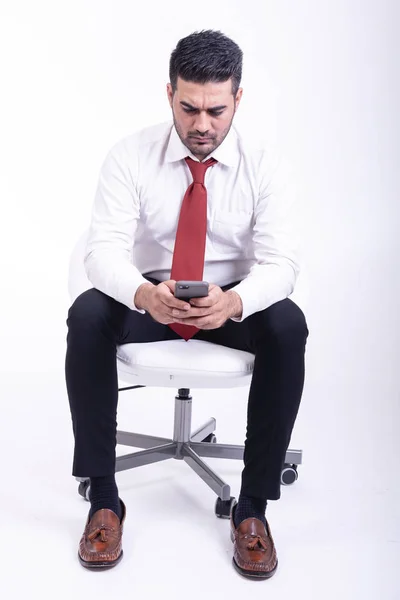 分離された白い椅子の上に座っての実業家 携帯電話 フォーカスを使用してハンサムな若いインドのビジネスマンに見えます 全身ショット — ストック写真