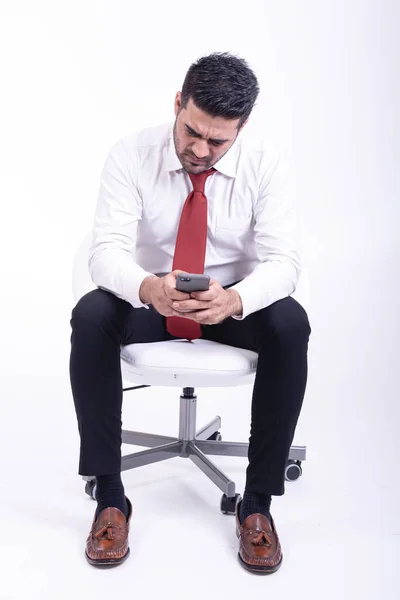 分離された白い椅子の上に座っての実業家 携帯電話 非常にフォーカスを使用してハンサムな若いインドのビジネスマンに見えます 全身ショット — ストック写真