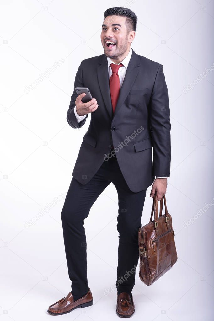 Businessman isolated. Handsome young indian businessman in suit with bag on phone portrait, very happy looks. Full length shot.