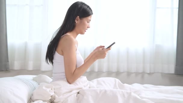 女性は ベッドでのショッピングします アジアの女性の店オンラインでクレジット カードでキーにベッドに座って携帯電話を使用して オンライン ショッピングの概念 — ストック動画