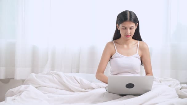 興奮した若いアジア女性のベッドに座っているとラップトップを使用して — ストック動画