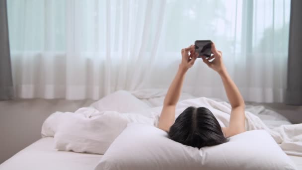 若いアジア女性ベッドに敷設し スマート フォンを使用して — ストック動画