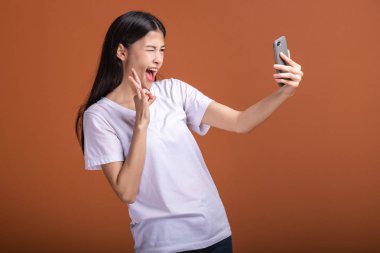 Cep telefonuyla turuncu arka plan üzerinde izole kadın. Asyalı kadın beyaz tişört içinde selfie poz. Hipster yaşam tarzı kavramı.