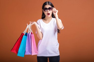 Alışveriş çantası turuncu arka planda izole tutan kadın. Beyaz t-shirt, şok ruh hali içinde Genç Asyalı kadın. Alışveriş kavramı.
