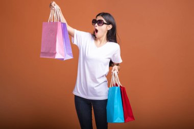 Alışveriş çantası turuncu arka planda izole tutan kadın. Beyaz t-shirt, şok ruh hali içinde Genç Asyalı kadın. Alışveriş kavramı.