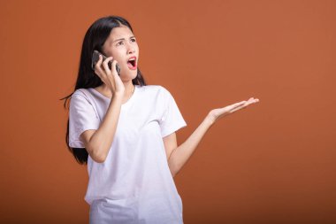 Cep telefonuyla turuncu arka plan üzerinde izole kadın. Asyalı kadın beyaz t-shirt, poz, avuç şok. Hipster yaşam tarzı kavramı.