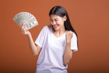 Turuncu arka planda izole nakit notlar tutan kadın. Heyecanlı kazanan poz, beyaz t-shirt doları not tutan Genç Asyalı kadın. Genç zengin hipster kavramı.