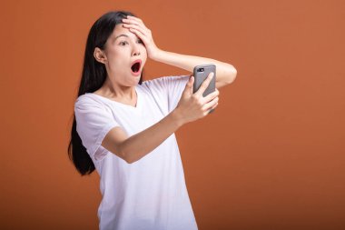 Cep telefonuyla turuncu arka plan üzerinde izole kadın. Asyalı kadın beyaz t-shirt, şok poz, kafasına ver. Hipster yaşam tarzı kavramı.