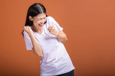 Turuncu arka plan üzerinde izole kadın kazanmak. Genç Asyalı hipster kadında büyük kazanmak çığlık poz ile beyaz t-shirt, iki el kaldırsın. Başarılı genç hipster kavramı.