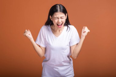 Turuncu arka plan üzerinde izole kadın kazanmak. Genç Asyalı hipster kadında büyük kazanmak çığlık poz ile beyaz t-shirt, iki el kaldırsın. Başarılı genç hipster kavramı.