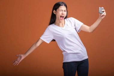 Cep telefonuyla turuncu arka plan üzerinde izole kadın. Asyalı kadın beyaz tişört içinde selfie poz. Hipster yaşam tarzı kavramı.