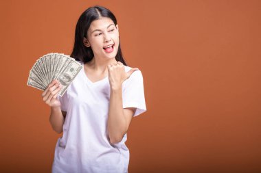 Turuncu arka planda izole nakit notlar tutan kadın. Genç Asyalı kadın heyecan ruh hali, beyaz t-shirt başparmak alana işaret içinde. Genç zengin hipster kavramı.