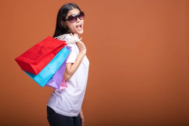 Alışveriş çantası turuncu arka planda izole tutan kadın. Beyaz t-shirt, mutlu ruh hali içinde Genç Asyalı kadın. Alışveriş kavramı.