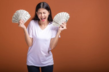 Turuncu arka planda izole nakit notlar tutan kadın. Büyük zafer çığlığı, beyaz t-shirt doları not tutan Genç Asyalı kadın. Genç zengin hipster kavramı.