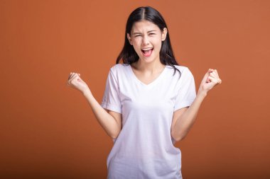 Turuncu arka plan üzerinde izole kadın kazanmak. Genç Asyalı hipster kadında büyük kazanmak çığlık poz ile beyaz t-shirt, iki el kaldırsın. Başarılı genç hipster kavramı.