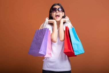 Alışveriş çantası turuncu arka planda izole tutan kadın. Beyaz t-shirt, çok mutlu ruh hali, çanta yüz yakınındaki Genç Asyalı kadın. Alışveriş kavramı.