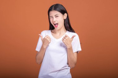 Turuncu arka plan üzerinde izole kadın kazanmak. Beyaz t-shirt ile kendinden emin poz, iki el zam, kadında Genç Asyalı hipster yaşasın. Başarılı genç hipster kavramı.