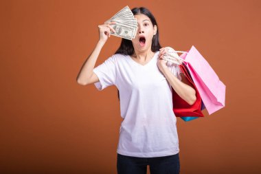 Alışveriş çantası ve turuncu arka planda izole para tutan kadın. Beyaz tişört çok şok ruh hali içinde Genç Asyalı kadın. Tatil alışveriş kavramı.